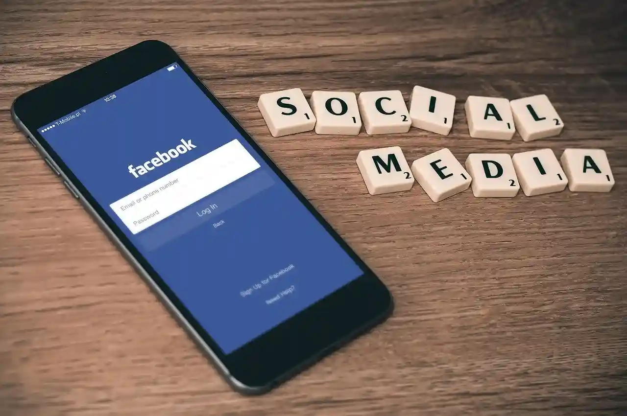 Facebook app open on phone with scrabble tiles spelling Social Media on wooden table — represents social media marketing concept